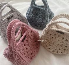 four crocheted purses sitting on top of a white bed next to each other