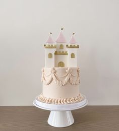 a white cake with pink frosting and gold trimmings sits on a pedestal