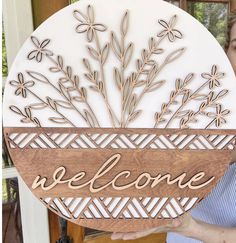 a woman holding up a welcome sign in front of a wooden plaque that says welcome