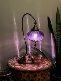 a purple lamp sitting on top of a table next to a potted green plant