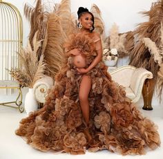 a pregnant woman sitting on top of a couch in a dress with feathers all over it