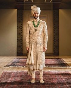 a man in a white turban and green tie standing on top of a rug