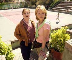 two women standing next to each other in front of a tennis court with people on it