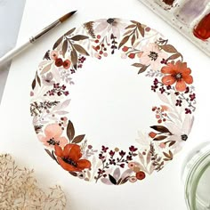 a paper plate with flowers painted on it next to paintbrushes and watercolor paints