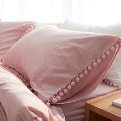 a pink pillow with pom - poms on it is sitting on a bed