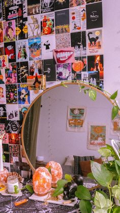 a mirror sitting on top of a table next to a potted plant in front of a wall covered with pictures