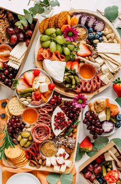 an assortment of cheeses, fruit and crackers are arranged on two platters