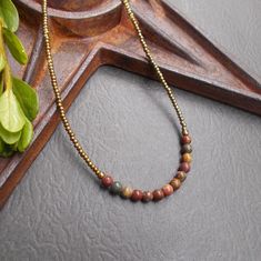 This is a dainty beaded necklace in a combination of earthy red creek jasper stones and tiny bronze seed beads. The stones include shades of red, green, ochre and tan - each stone is unique. The necklace is finished with an antiqued brass plated hook and eye clasp. You can add an optional brass plated 2-inch extender chain for added versatility or peace of mind if this is a gift. This earthy necklace is casual enough for everyday wear. It is lightweight and the optional extender chain would make it easy to layer with some other faves. Necklace length: approx. 16"; optional 2" extender chain available Beaded Necklace Collection: https://www.etsy.com/shop/BonArtsStudio?ref=seller-platform-mcnav&section_id=17053954 See What's New: https://www.etsy.com/shop/BonArtsStudio?ref=seller-platform-mc Bronze Beaded Necklace With Polished Beads As Gift, Beaded Necklaces With Gemstone And Brass Round Beads, Brass Beaded Necklaces With Gemstone Beads, Brass Beaded Necklace With Gemstone Beads, Brass Necklaces With Round Natural Stone Beads, Brass Round Beads Necklace With Natural Stones, Brass Necklace With Round Natural Stone Beads, Earthy Bronze Beaded Jewelry, Earthy Bronze Jewelry With Round Beads