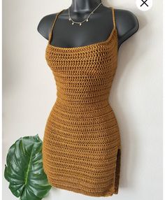 a crocheted dress on a mannequin with a green plant in the foreground