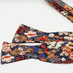 Floral Bow Tie. Blue, Muted Red, Tan Small Print. - Self-tie. Hand-stitched from the 100% cotton, Liberty of London. - Bow Tie measures approx. 4.5" x 2.25" when tied. - The strap is adjustable and accommodates neck sizes up to 18.5" - Packaged in the signature box, perfect for the gift. - Would work great for the classic blue, copper and red wedding theme, special occasion or an everyday outfit. - Matching pocket square: https://www.etsy.com/ca/listing/730071822/floral-pocket-square-red-copper- Fitted Casual Cotton Ties, Casual Fitted Cotton Ties, Red Fitted Summer Tie, Elegant Multicolor Wedding Ties, Floral Bowtie Groomsmen, Floral Bow Tie Wedding Groomsmen, Multicolor Floral Print Wedding Ties, Red Summer Bow Tie, Blue Floral Bow Tie