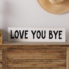 a wooden sign that says love you bye on top of a dresser next to a hat