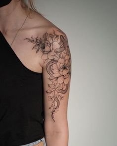 a woman with a flower tattoo on her left arm and shoulder is standing in front of a white wall