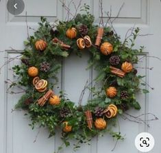 a wreath with oranges and pine cones hanging on the front door to decorate it