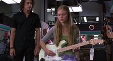 two young people are playing guitars in a music store, one is wearing headphones and the other is holding a guitar