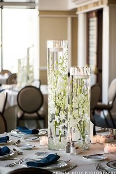 two tall vases filled with flowers sitting on top of a table covered in plates and silverware