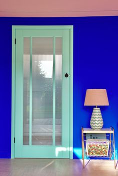 a room with blue walls and a white table in front of the door that has a lamp on it