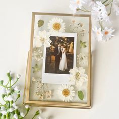 a wedding photo frame with flowers and daisies on the table next to it is an image of a bride and groom