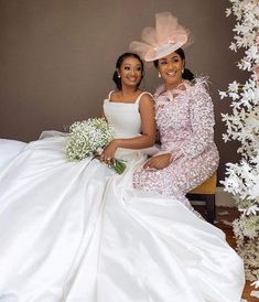 two women in white dresses sitting next to each other on a chair with flowers around them