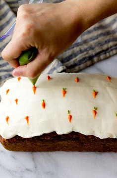 a person is decorating a cake with white frosting and carrots on it