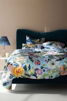 a bed with a blue headboard and floral comforter on it in a bedroom