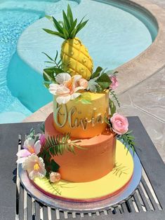 there is a cake with flowers and pineapples on it next to the pool