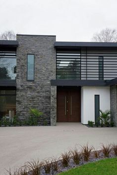 a modern house with stone and wood sidings on the front door, along side a large driveway