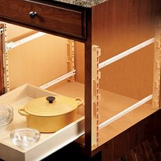 a yellow pot is sitting on the bottom shelf of a kitchen cabinet with glass bowls