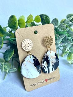 the marble and gold earrings are on display next to some green leaves, with a tag that says handmade with love