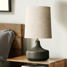 a lamp on a night stand next to a bed with a wooden headboard and nightstand