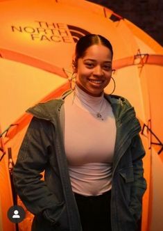 a woman standing in front of an orange tent with the north face logo on it