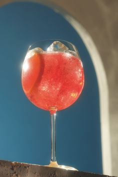 a red drink sitting on top of a wooden table next to a blue wall and window