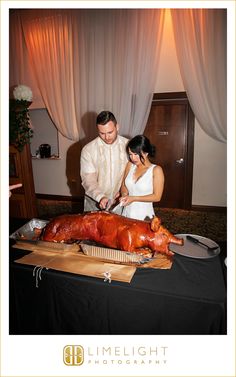 a man and woman cutting up a large piece of meat on top of a table