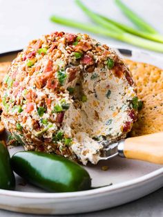 a white plate topped with crackers and cheese ball covered in toppings next to green peppers