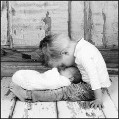 a black and white photo of a child kissing a baby