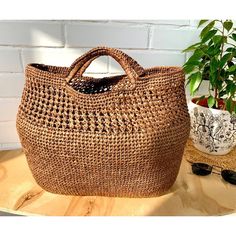 a woven bag sitting on top of a wooden table next to a potted plant