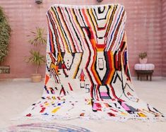 a multicolored rug on the ground in front of a brick wall and potted plant