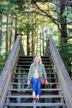 a woman sitting on top of a wooden staircase in the woods with trees behind her