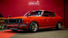 an orange muscle car parked in front of a red wall