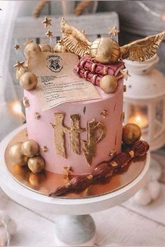 a pink and gold birthday cake with an angel decoration on top is sitting on a table