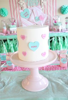 a white cake sitting on top of a table covered in pink and blue paper hearts