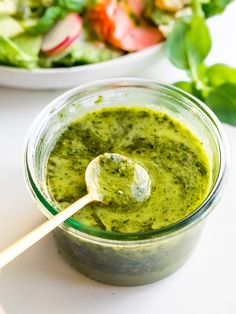 a glass jar filled with pesto sauce next to a bowl of salad and a wooden spoon