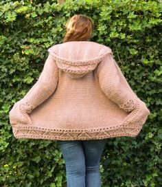 a woman standing in front of a hedge wearing a sweater with hoodie on it