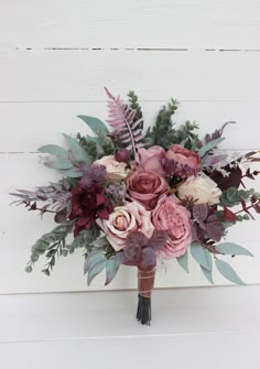 a bridal bouquet with pink and purple flowers on a white background, in front of a wood paneled wall