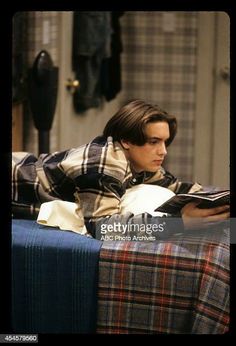 a young man laying on top of a bed reading a book