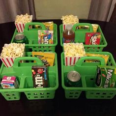 four green baskets filled with movie snacks and sodas on top of a black table