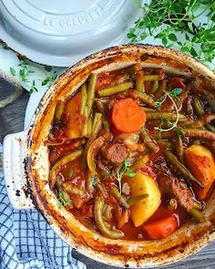 a pot filled with stew and vegetables on top of a wooden table next to a blue towel