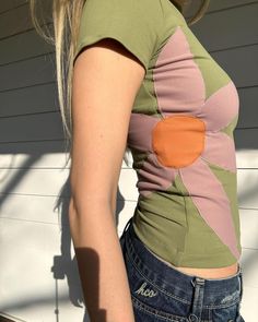 a woman with long blonde hair wearing a green shirt and blue jeans standing in front of a white wall