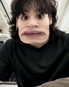 a man with long hair and black shirt making a funny face while sitting in front of a laptop computer