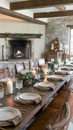 a long table with place settings and candles in front of an open fire place setting