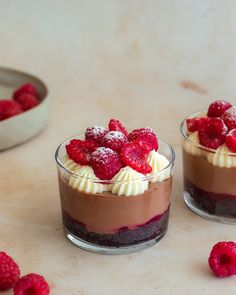 two desserts with raspberries and whipped cream on top are sitting on a table